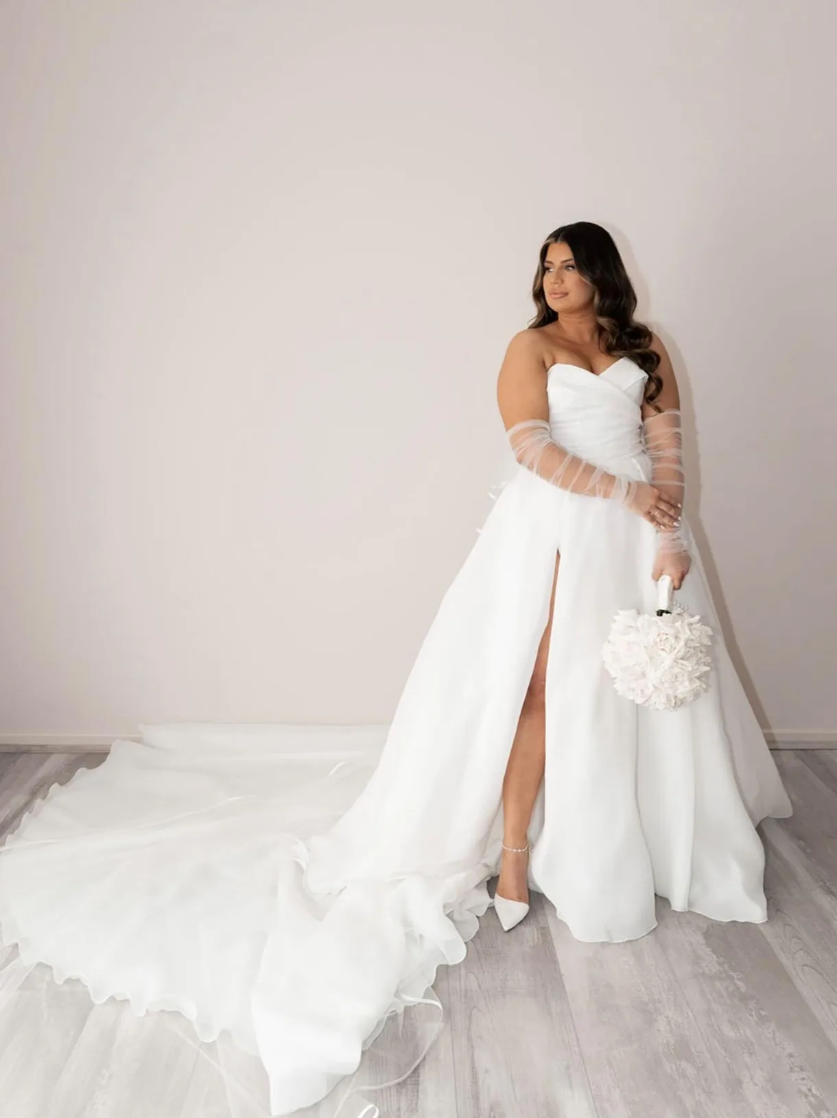 Bride full-length against a plain studio wall with a warm even tan