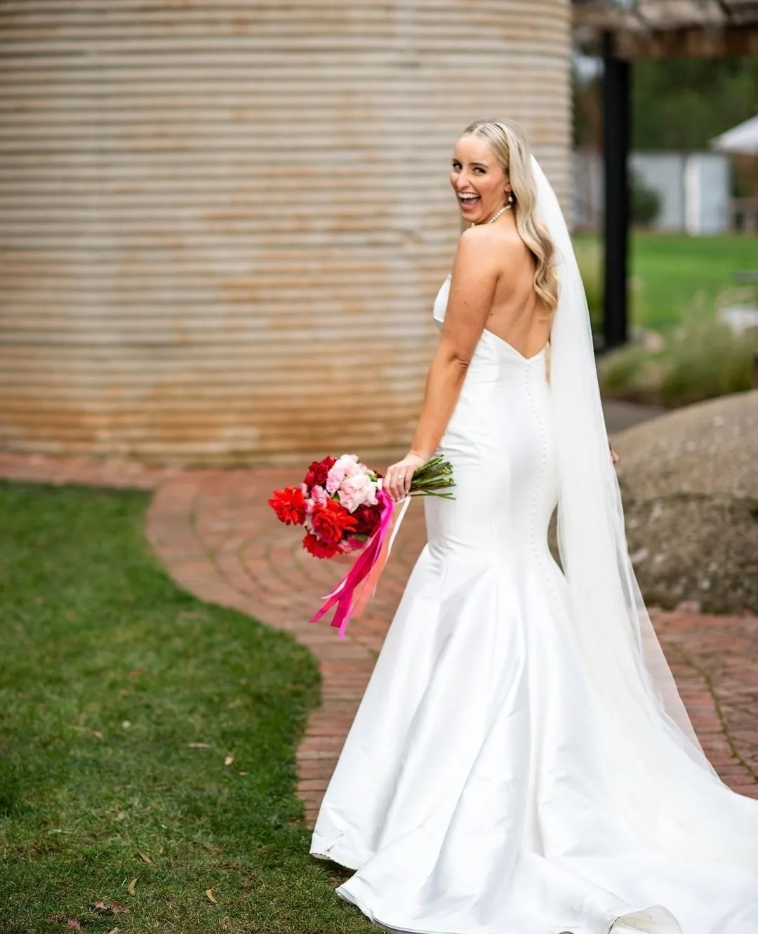 Blonde bride at a winery turning over her shoulder, bronzed bare back glowing
