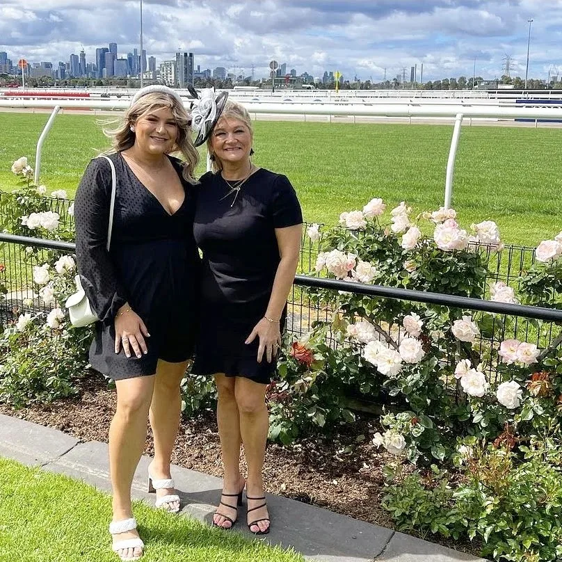 Two clients in black at Flemington racecourse, glowing against the city skyline