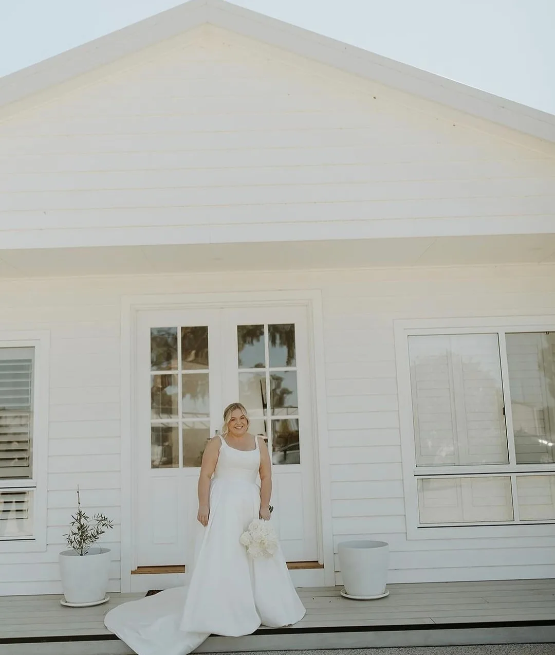 Bride glowing before a white weatherboard cottage on her wedding day