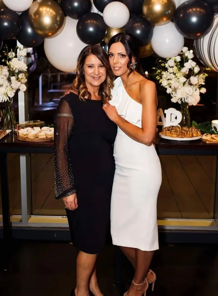Two clients at a black-and-gold balloon party, glowing beside a dessert table